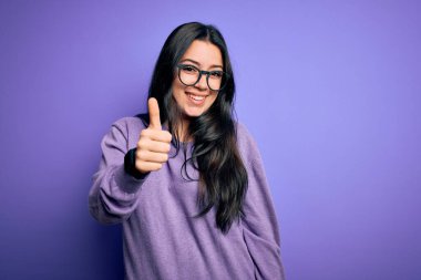 Mor izole arka planda gözlük takan esmer bir kadın mutlu bir el hareketi yapıyor. Kameraya bakıp başarıyı gösteren ifade onaylanıyor.