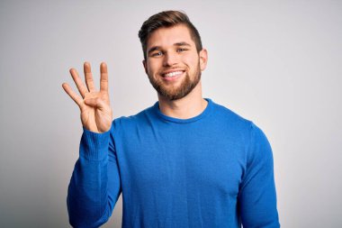 Young handsome blond man with beard and blue eyes wearing casual sweater showing and pointing up with fingers number four while smiling confident and happy.