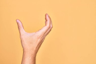 İzole edilmiş sarı arka plan üzerinde parmaklarını gösteren beyaz bir adamın eli. Görünmez bir şeyi alıp, parmaklarıyla uzayı gösteren bir nesneyi tutuyor.