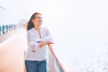Tatilde mutlu ve kendinden emin gülümseyen genç ve güzel bir kadın. Yüzünde gülümsemeyle bir gemi güvertesinde durmak.