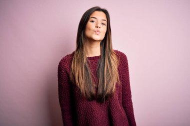 İzole edilmiş pembe arka plan üzerine sıradan bir süveter giyen genç ve güzel bir kız canlı yayında öpüşürken kameraya bakıyor ve sevimli ve seksi oluyor. Aşk ifadesi.