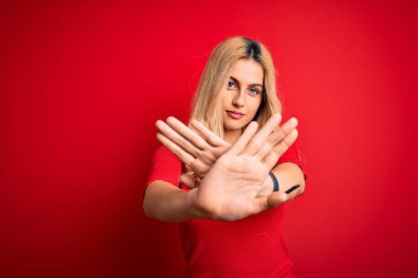 Genç, güzel, sarışın bir kadın. Günlük tişört giyiyor. Kırmızı arka plan üzerinde duruyor.