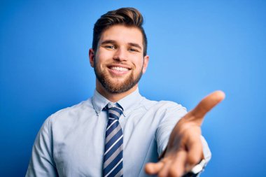 Sarışın, sakallı, mavi gözlü, şık gömlekli ve kravatlı genç bir işadamı. Karşılama ve hoş geldin demek için gülümseyerek tokalaşıyor. Başarılı bir iş..