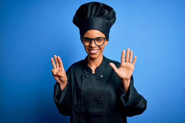 年轻的非洲女厨师身穿炊具制服 头戴蓝色背景的帽子 带着八号手指 面带微笑 自信而快乐 — 图库照片