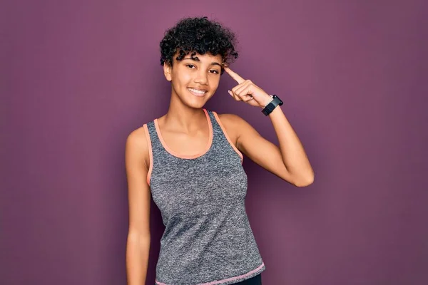 年轻美丽的非洲裔美国女运动员穿着运动服做运动 微笑着用一个手指指着头 很好的主意或想法 好的记忆力 — 图库照片