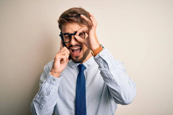 Genç işadamı beyaz arka planda akıllı telefondan konuşuyor. Gülümsüyor. El ele imzala ve parmaklarından bak.