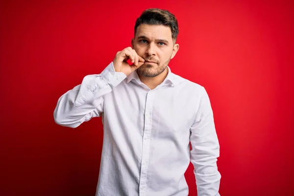 Young business man with blue eyes wearing elegant shirt standing over red isolated background mouth and lips shut as zip with fingers. Secret and silent, taboo talking
