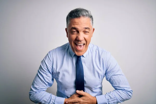 Middle age handsome grey-haired business man wearing elegant shirt and tie smiling and laughing hard out loud because funny crazy joke with hands on body.