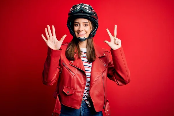 若い美しいブルネットのオートバイのヘルメットと赤いジャケットを身に着けているオートバイの女性が表示され 指番号8で指摘しながら 自信と幸せ笑みを浮かべて — ストック写真