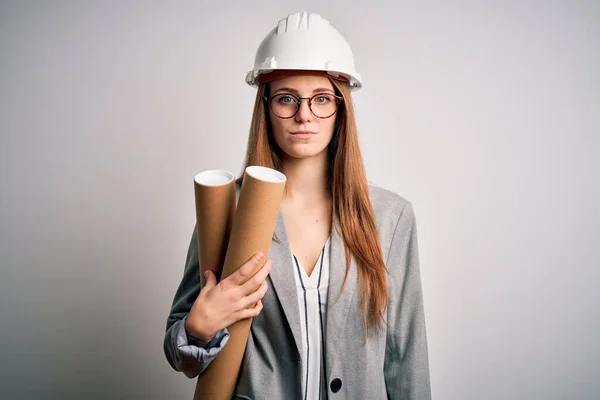 年轻美丽的红头发女建筑师 戴着眼镜 头戴安全帽 手里拿着设计图 脸上带着自信的表情 一副严肃严肃的表情 — 图库照片