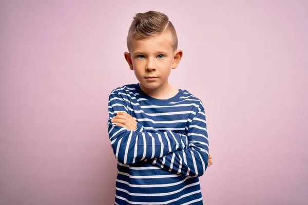 ピンクの背景にネイビーのストライプのシャツを着た青い目の若い白人の子供は懐疑的で緊張し 両腕を組んで顔に不承認の表現 負の人 — ストック写真