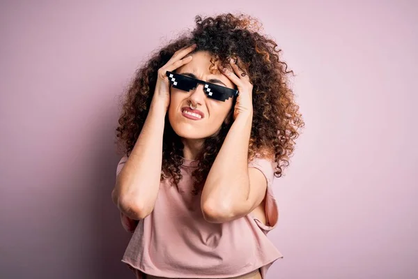 stock image Young beautiful woman with curly hair and piercing wearing funny thug life sunglasses suffering from headache desperate and stressed because pain and migraine. Hands on head.