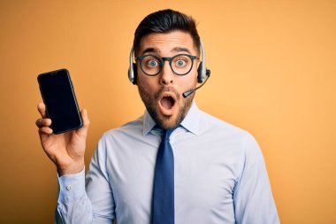 Çağrı merkezinden gelen müşteri hizmetleri kulaklığı olan bir işletmeci şok olmuş, korkmuş ve korku ifadesinden heyecanlanmış bir halde akıllı telefon ekranı gösteriyor.