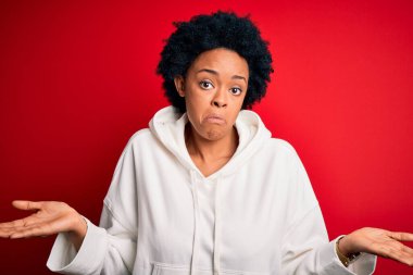 Kıvırcık saçlı, spor giyimli, kafası karışık ve kolları ve elleri havada genç, Afro-Amerikan bir afro kadın. Şüphe kavramı.