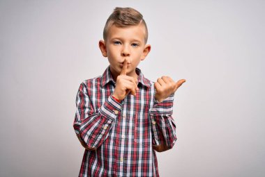 Mavi gözlü, zarif gömlekli, izole edilmiş arka planda duran küçük beyaz bir çocuk ellerini yan tarafa uzatarak dudaklarını işaret ederek sessiz olmasını istiyor. Sessizlik ve gizli konsept.