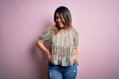 Moda kıyafetleri giyen genç ve güzel bir kadın. Manken, sokak tarzı giyiniyor. Pembe arka planda dikiliyor.