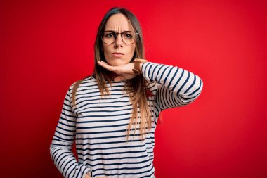 Kırmızı arka planda duran gözlüklü, sarışın, genç, güzel bir kadın bıçakla boğazını kesiyor, saldırganlığı şiddetle tehdit ediyor.