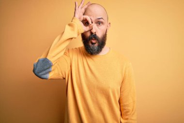Sarı arka planda dikilen sıradan süveter giyen sakallı yakışıklı kel adam şaşırmış yüz ifadesiyle şaşırmış, parmaklarından bakan gözler. İnançsız ifade.