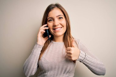 Akıllı telefondan konuşan genç bir kadın izole edilmiş arka planda mutlu bir şekilde gülümsüyor.