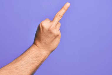 Hand of caucasian young man showing fingers over isolated purple background showing provocative and rude gesture doing fuck you symbol with middle finger