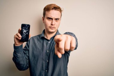 Genç, yakışıklı, elinde kırık bir akıllı telefon tutan, kamerayı işaret eden kırık bir ekran gösteren, kendine güvenen, ciddi bir jest yapan bir adam.