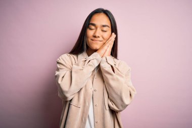 Genç, güzel Asyalı bir kadın pembe arka planda dikilmiş, uyur, yorgun düşler kurar, elleri ile poz verir ve gözleri kapalı gülümserdi..