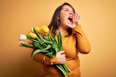 Sarı arka planda romantik lale çiçekleri tutan ve el ele tutuşarak bağıran güzel, iri yarı bir kadın. İletişim konsepti.