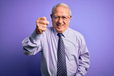 Gri saçlı, gözlüklü yaşlı bir iş adamı, mor izole edilmiş arka planda dikiliyor kızgın ve kızgın bir şekilde yumruğunu kaldırıyor ve öfkeyle bağırıyor. Öfke ve agresif kavram.