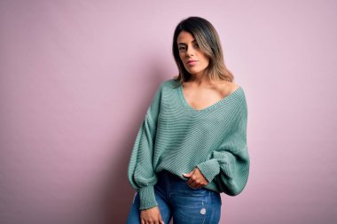 Moda kıyafetleri giyen genç ve güzel bir kadın. Manken, sokak tarzı giyiniyor. Pembe arka planda dikiliyor.