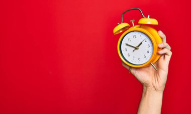 Güzel bir el, izole edilmiş kırmızı arka plan üzerinde klasik çalar saat tutan bir adam.