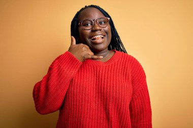 Sarı arka planda normal süveter giyen, el ve parmaklarıyla telefonla konuşan Afro-Amerikan kadın. İletişim kavramları.