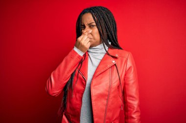Genç Afro-Amerikalı bir kadın kırmızı izole edilmiş arka planda havalı bir deri ceket giyiyor. Kokuşmuş ve iğrenç bir koku alıyor. Dayanılmaz bir koku. Kötü kokuyor.