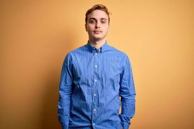 İzole edilmiş sarı arka plan üzerine sıradan çizgili tişört giyen genç ve yakışıklı bir adam. Yüzünde ciddi bir ifadeyle rahatlamış. Basit ve doğal bir şekilde kameraya bakıyorsun..