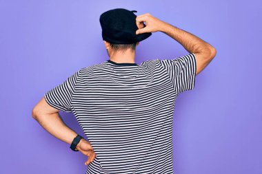 Mavi gözlü, çizgili tişört giyen ve mor arka planda Fransız beresi takan yakışıklı bir adam. Geriye doğru, elleri kafasında şüpheyi düşünüyor.