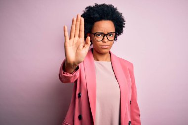 Young beautiful African American afro businesswoman with curly hair wearing pink jacket doing stop sing with palm of the hand. Warning expression with negative and serious gesture on the face. clipart