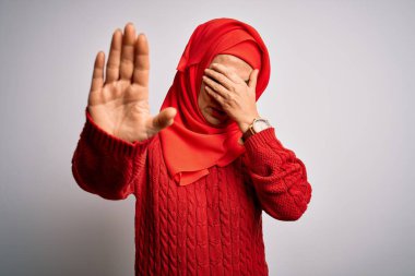 Orta yaşlı esmer kadın izole edilmiş beyaz arka plan üzerine geleneksel tesettür takıyor gözleri ellerle örtüyor ve üzgün ve korku ifadeleriyle dur hareketi yapıyor. Utanç verici ve olumsuz bir kavram..