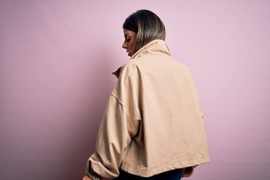 Moda kıyafetleri giyen genç ve güzel bir kadın. Manken, sokak tarzı giyiniyor. Pembe arka planda dikiliyor.