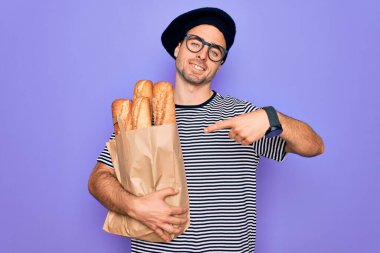 Mavi gözlü genç fırıncı Fransız beresi takıyor. Yanında ekmek çantası var. Elle ve parmakla göstererek çok mutlu.