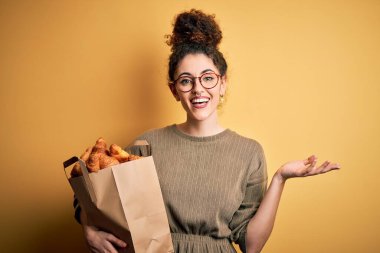 Kıvırcık saçlı ve elinde kruvasanlarla kruvasan tutan güzel bir kadın. Çok mutlu ve heyecanlı. Kazanan ifade zaferi büyük bir gülümsemeyle kutluyor ve ellerini kaldırıyor.