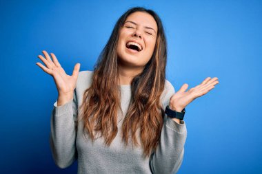 Genç, güzel esmer kadın mavi arka planda dikilmiş çılgın ve çılgın başarısını kutluyor kolları havada ve gözleri kapalı heyecanla bağırıyor. Kazanan konsept