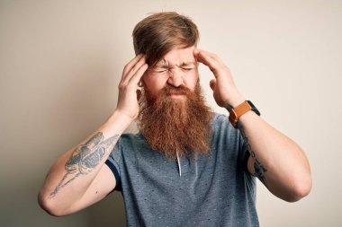 Sakallı ve kolunda dövmesi olan yakışıklı İrlandalı bir adam izole edilmiş bir arka planda duruyor. Baş ağrısı, acı ve migren yüzünden stres altında. Ellerini başının üstüne koy..
