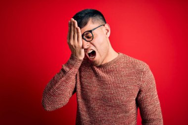 Kırmızı arka planda inek gözlüğü takan genç, yakışıklı İspanyol adam esnemekten yoruldu. Yüzün yarısını, gözünü ve ağzını eliyle kapattı. Yüzüm acıyor..