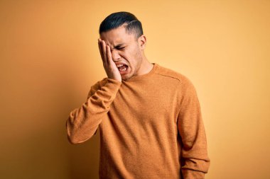 İzole edilmiş sarı arka planda dikilen sıradan süveter giyen genç Brezilyalı adam yarı yüz, göz ve ağız kısmını eliyle kapatmaktan yoruldu. Yüzüm acıyor..