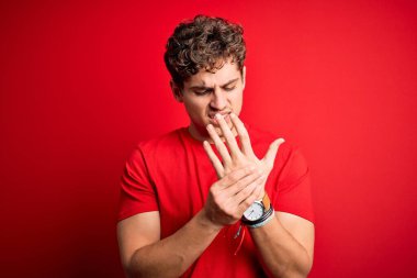 Sarışın, kıvırcık saçlı, kırmızı arka planda günlük tişört giyen elleri ve parmakları ağrıyan, eklem iltihabı olan genç bir adam.