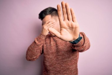 Pembe izole edilmiş arka plan üzerine sıradan bir kazak giyen genç, yakışıklı, beyaz bir adam ellerle gözlerini kapatıyor ve üzgün ve korku ifadeleriyle hareketlerini durduruyor. Utanç verici ve olumsuz bir kavram..