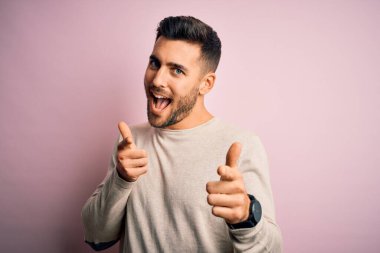 İzole edilmiş pembe arka planda dikilip mutlu ve komik yüzlü genç ve yakışıklı bir adam. İyi enerji ve titreşimler.