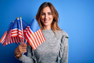 Amerika Birleşik Devletleri bayraklarını tutan genç, güzel, vatansever bir kadın. Mutlu bir yüzle bayrak kaldırıyor. Kendine güvenen bir gülümsemeyle dişlerini gösteriyor.