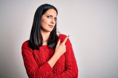 Mavi gözlü genç esmer kadın izole edilmiş beyaz arka plan üzerine gündelik süveter giyiyor. El parmağı ile reklamını yapıyor, ciddi ve sakin bir yüz ifadesi var.