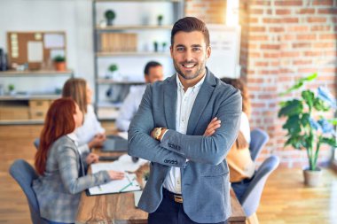 Group of business workers working together. Young handsome businessman standing smiling happy looking at the camera at the office