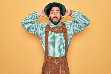 Almanya festivali için geleneksel Alman Ekim Festivali kıyafeti giyen genç yakışıklı adam elleri başında çılgın ve korkmuş, ağzı açık şoktan korkmuş ve şaşırmış.